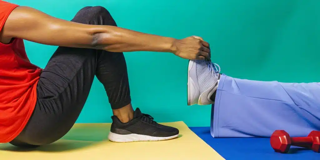 A person receives an assisted dynamic leg stretch from a partner for a warm-up.