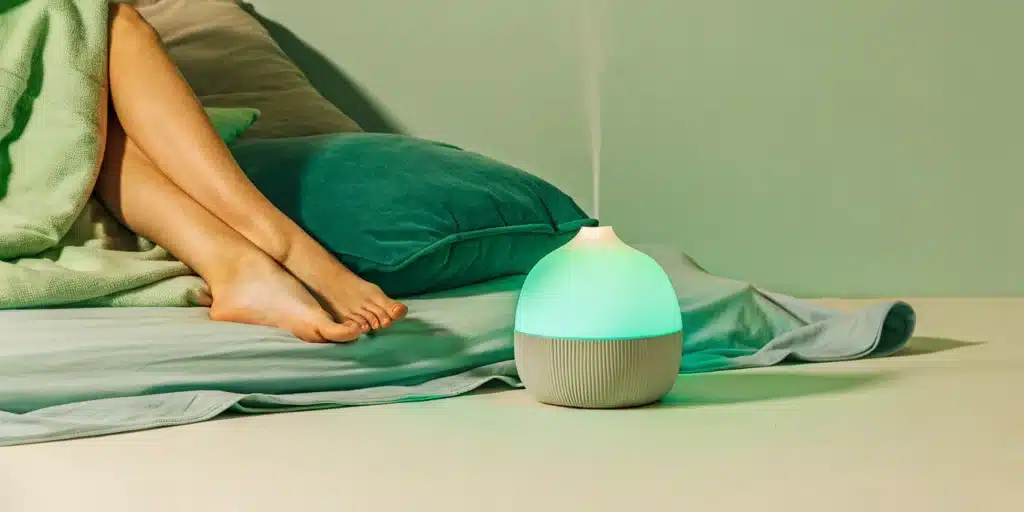 A woman relaxes her leg muscles at night by stretching in bed with an aromatherapy diffuser.