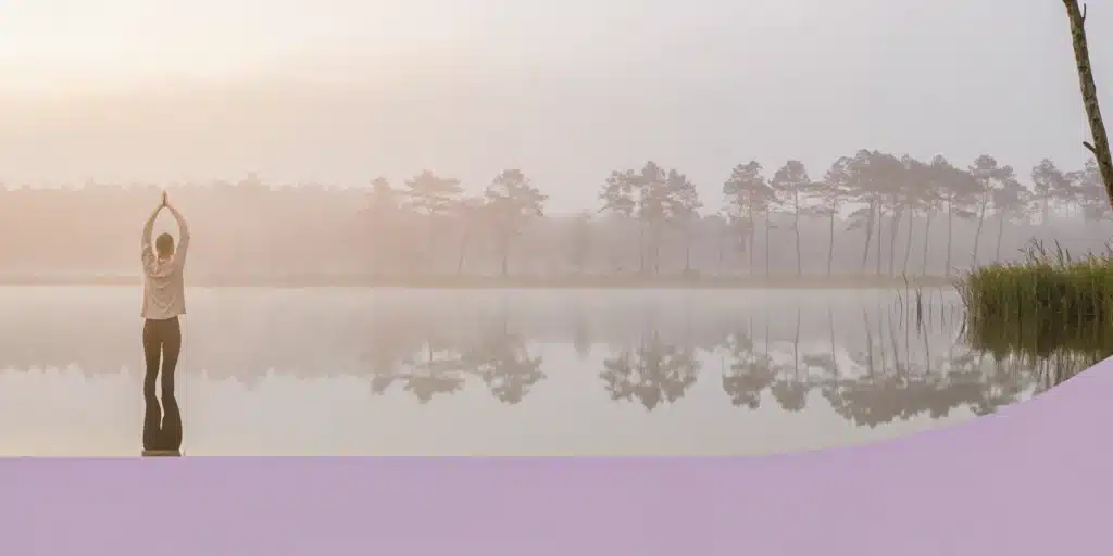 A person does gentle yoga by a lake, showing how to start exercising when everything hurts.