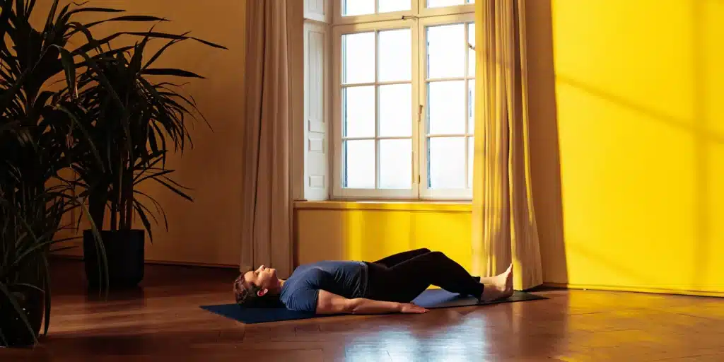 A person stretching on a mat to relieve stiff legs, a common sign of muscle strain.